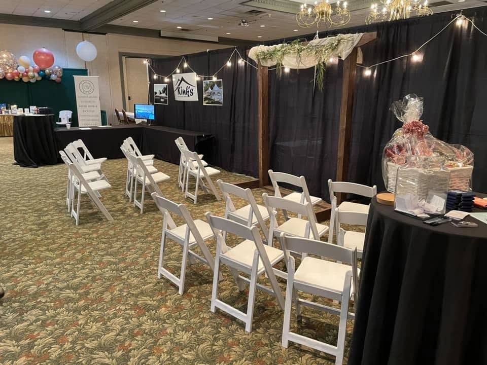 Kink's booth at a bridal show with white chairs and a wedding arch