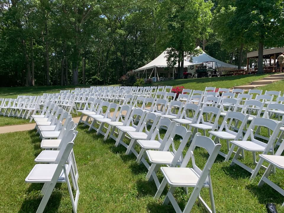 Rows of white padded chairs set on a lawn for an outdoor ceremony, with a pole tent behind