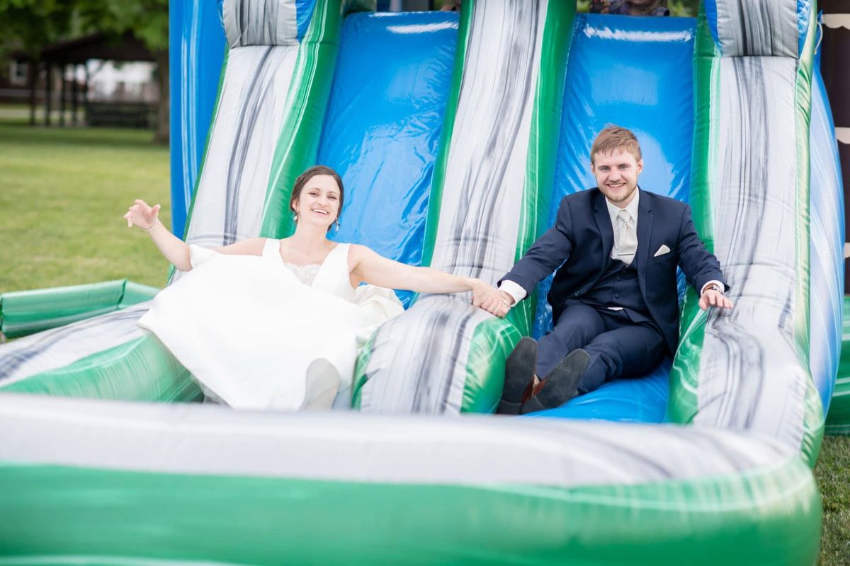 Bride and groom laughing at the bottom of an inflatable water slide