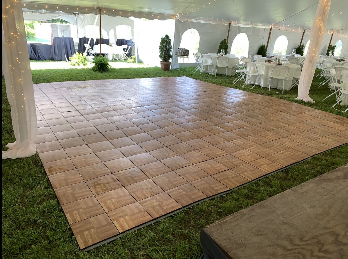 Wood parquet dance floor inside a pole tent with round tables and string lights