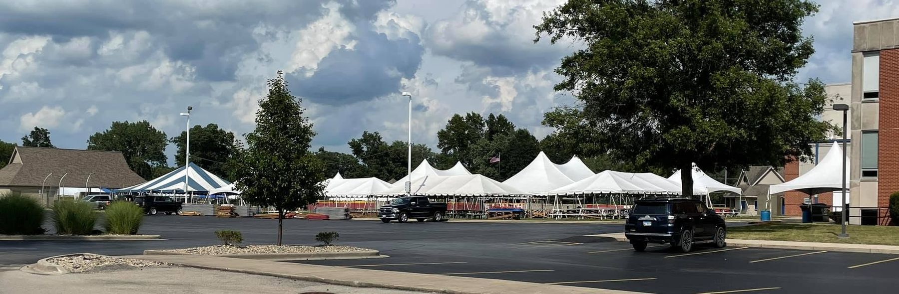 Row of white pole and high-peak tents set up across a parking lot for a community festival