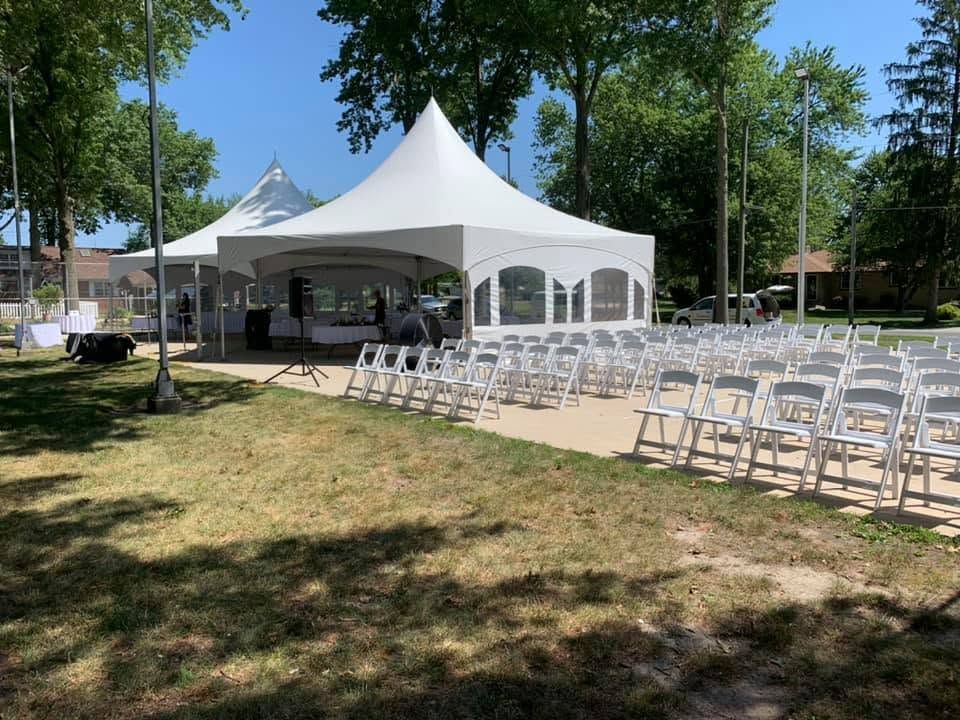 High-peak tents with ceremony chairs set up in a park