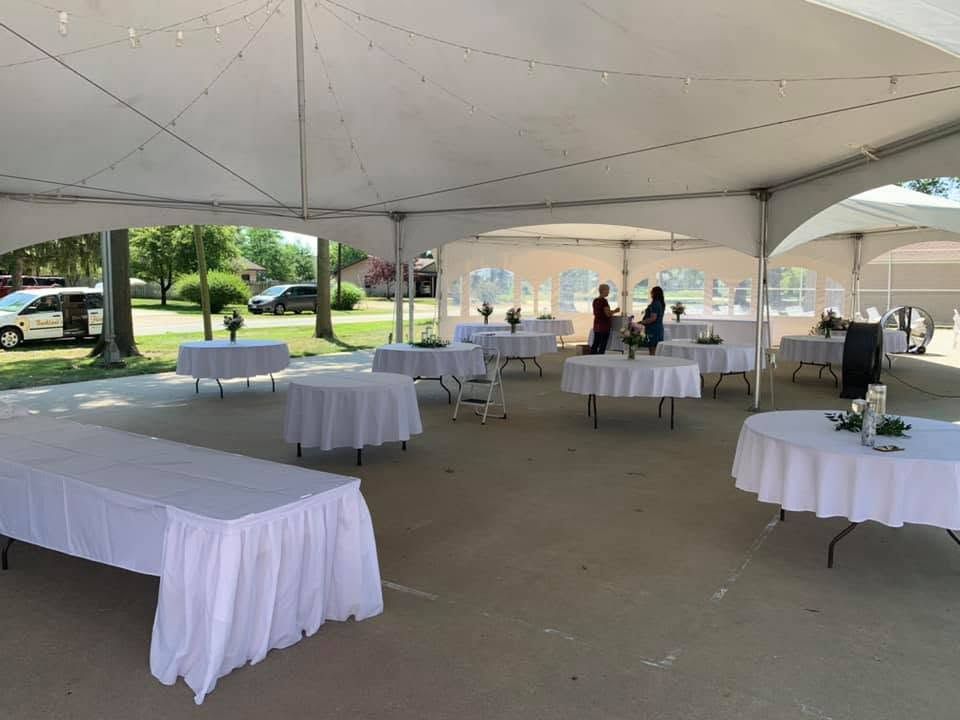 Round tables with white linens set up inside a high-peak tent