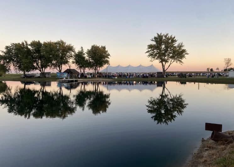 High-peak tent at a lakeside event at sunset