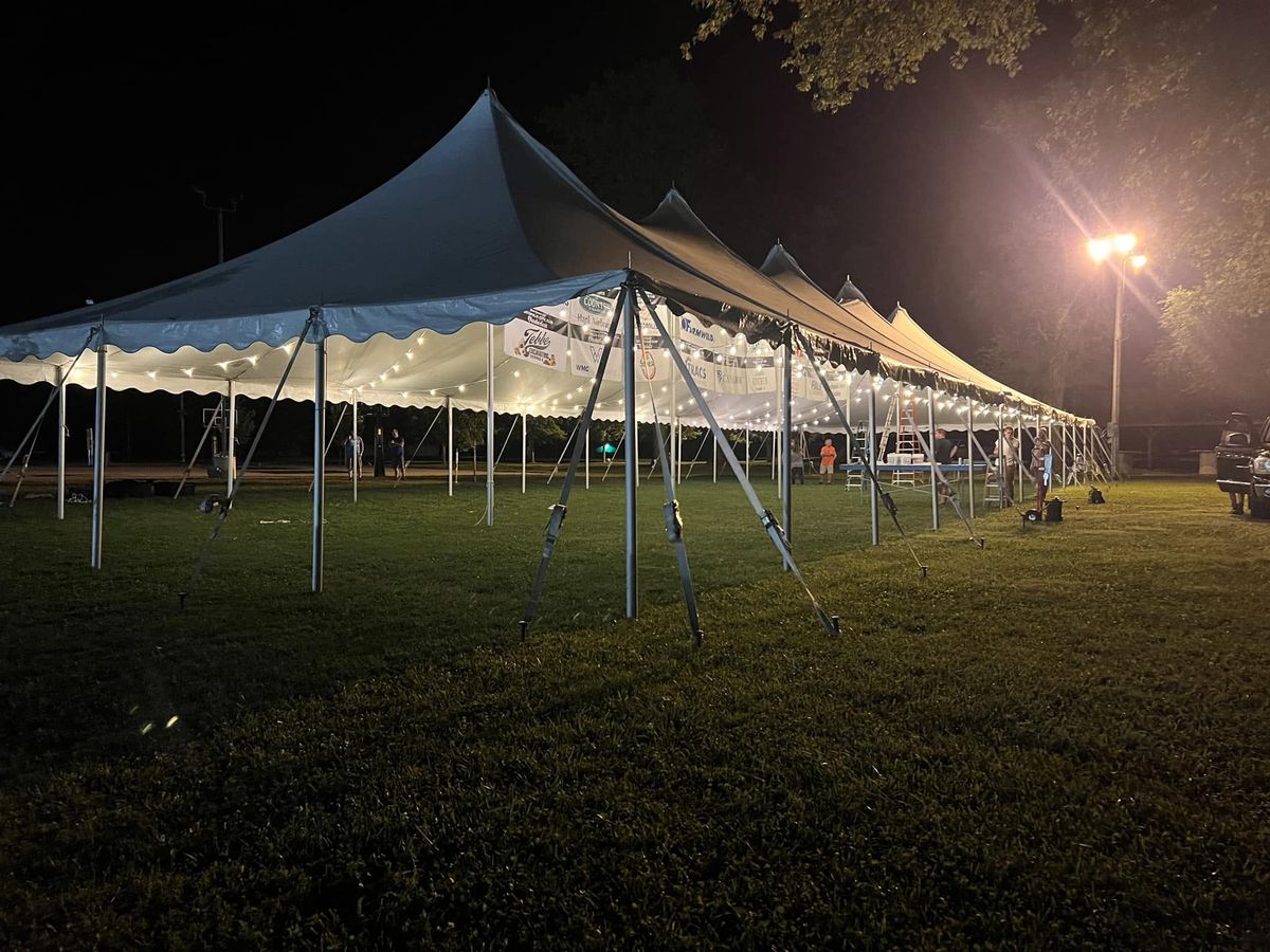 Long white pole tent lit with string lights at night
