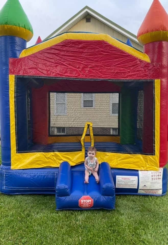 Toddler sitting on the entry slide of a rainbow castle bounce house