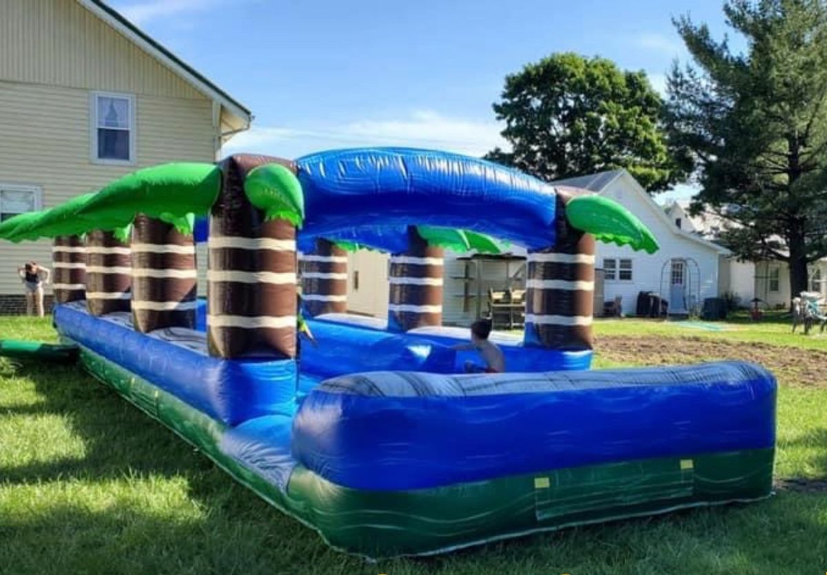 Child sliding through a palm-tree inflatable slip slide in a backyard